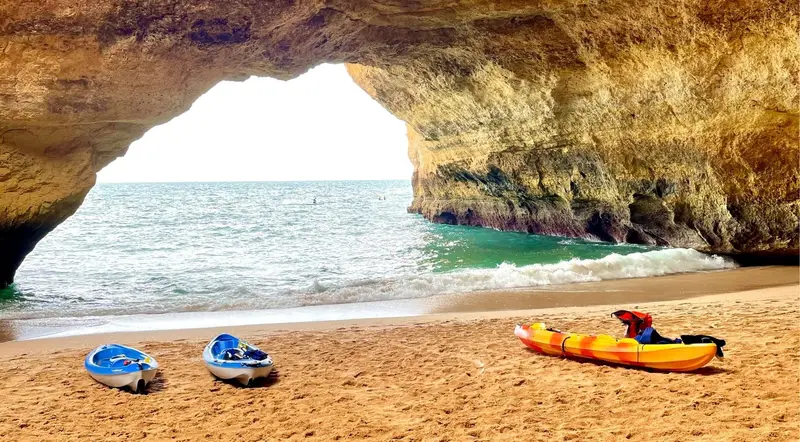 Kayaks on the sand beside a sea cave arch on a guided Benagil kayak tour