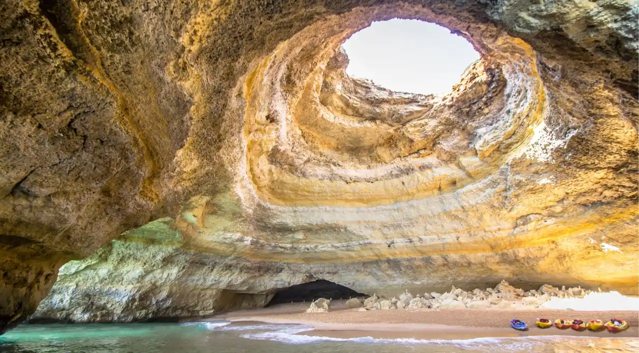 Sunlight pouring through the round skylight of Benagil Cave onto its golden inner beach and turquoise water