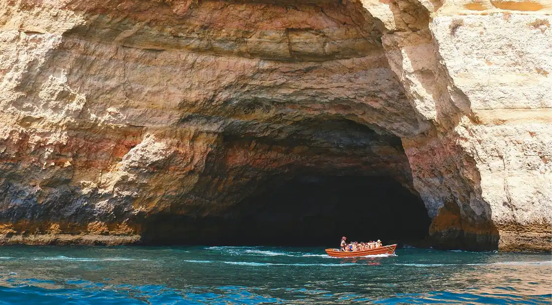 A small boat entering the mouth of Benagil Cave below the golden Algarve cliffs