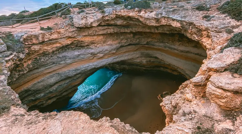 The fenced Benagil sinkhole skylight seen from the clifftop viewpoint above the cave